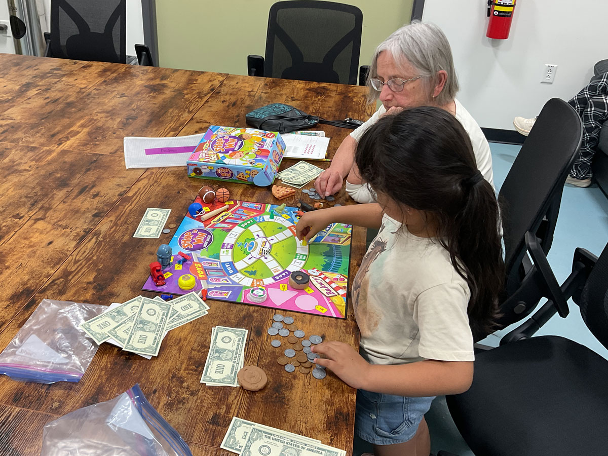 A child and tutor play a shopping game with pretend money